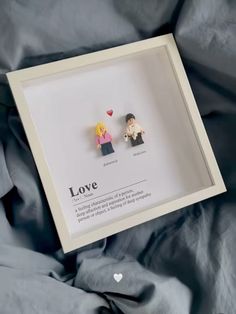 two miniature people are sitting in a shadow box with the word love written on it