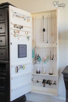 a jewelry cabinet is open to show necklaces and bracelets on the wall above it