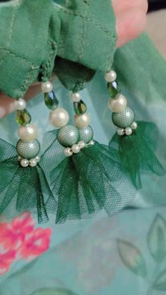 a pair of earrings with green leaves and pearls on them are being held by someone's hand