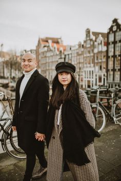 two people standing next to each other in front of some buildings and bicycles on the street