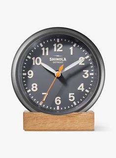 an analog clock sitting on top of a wooden stand in front of a white background