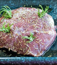 a piece of raw meat with rosemary sprigs on it in a roasting pan