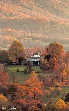 a large white house surrounded by trees in the middle of a field with mountains in the background