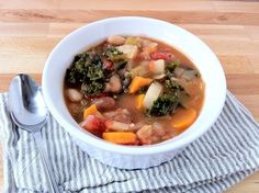 a white bowl filled with vegetable soup on top of a wooden table next to a spoon