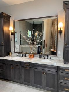 a bathroom vanity with two sinks and large mirror over it's top, surrounded by dark wood cabinets