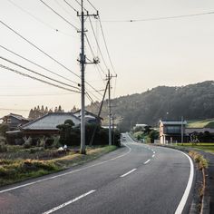 an empty road with power lines above it and houses on the other side in the distance