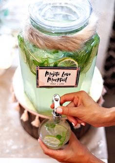 a person holding a jar filled with green liquid and limes on top of a table