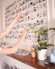 two women are placing pictures on the wall above a table with potted plants in front of them