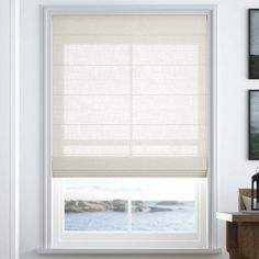 a window with white blinds in a room next to a table and pictures on the wall