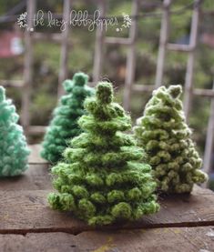 three small knitted trees sitting on top of a wooden table