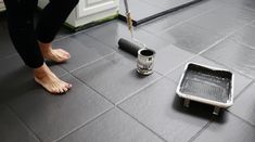 a person standing next to a floor grout with a paint roller in front of it