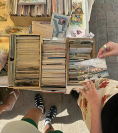 two people sitting at a table with many books and magazines on it, one person is reading