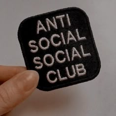 a hand holding up a black and white patch with the words anti social social club on it