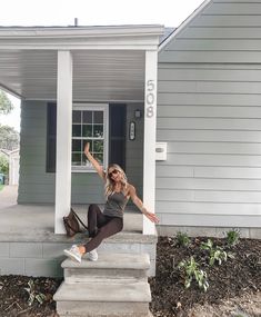 a woman sitting on steps in front of a house with her arms up and legs crossed