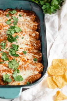 a green casserole dish with cheese, sauce and cilantro on top