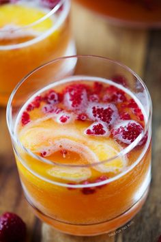 two glasses filled with orange and raspberry punch on top of a wooden table