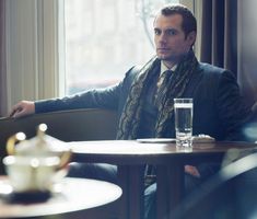 a man sitting at a table with a drink in front of him and looking off into the distance