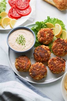 crab cakes on a plate with dipping sauce and lemon wedges next to the plate