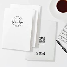 a cup of coffee next to two notebooks and a keyboard on a white table