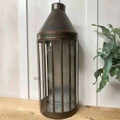 a metal lantern sitting on top of a wooden table next to a potted plant