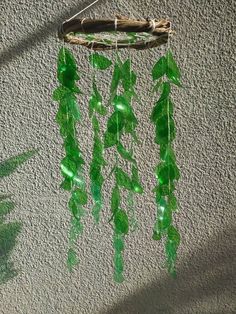 a green glass wind chime hanging from a wall next to a potted plant