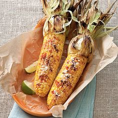 grilled corn on the cob with limes and spices in an orange bowl