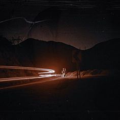 car lights streaking by on the road at night with mountains in the background and dark sky