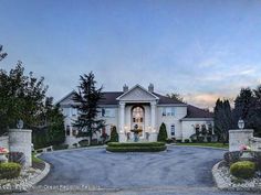 a large white house with two driveways and bushes in front of it at dusk