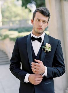 a man in a tuxedo is posing for the camera with his hands on his chest