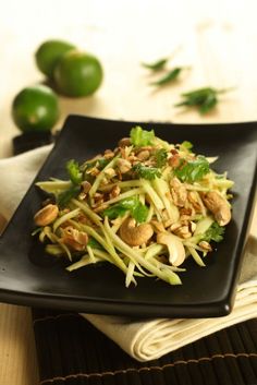 a black plate topped with green vegetables and nuts