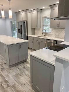 a kitchen with gray cabinets and white counter tops, an island in the middle is surrounded by stainless steel appliances