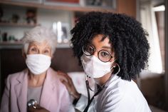 two women wearing face masks in the living room, one holding a stethoscope