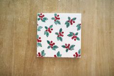 a napkin with holly and red berries on it sitting on top of a wooden table