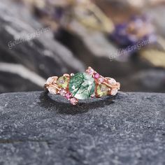 a ring with green and pink stones sitting on top of a rock