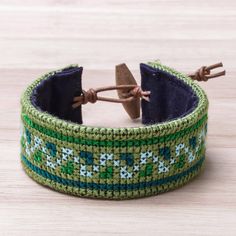 Featuring green cross-stitched patterns in the style of Hmong hill tribe handicrafts this cotton wristband bracelet from Thailand is designed by Nulee. She completes the bracelet with leather cord and an adjustable raintree wood button clasp. Hmong Embroidery, Hand Painted Jewelry, Wristband Bracelet, Green Jewelry, Shopping Ideas, Wooden Jewelry, Jewelry Packaging, Unique Necklaces, Leather Jewelry