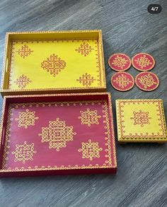 three trays and two coasters with designs on them sitting on a wooden table