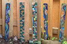 several colorful stained glass pieces are lined up against a wooden fence with plants in the foreground