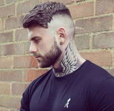 a man with tattoos on his neck standing in front of a brick wall