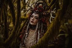 a woman with long dreadlocks standing in the woods wearing a deer headdress