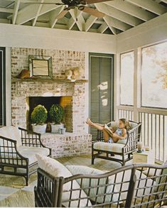 a woman sitting in a chair on top of a porch next to a fire place