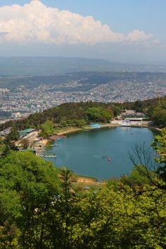 a large body of water surrounded by lush green trees and mountains in the distance is a city