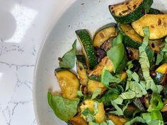 a white bowl filled with zucchini and spinach on top of a table