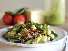 a white plate topped with pasta and asparagus next to some tomatoes on a table