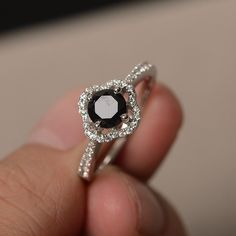 a close up of a person's hand holding a ring with a black and white diamond