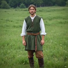 a man standing in a field wearing a green dress and brown boots with his hands on his hips