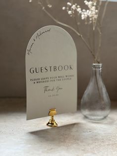 a vase with flowers in it next to a sign that says guestbook on it