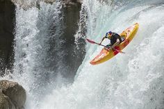 a man riding on top of a yellow kayak in front of a large waterfall