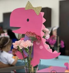 a vase with flowers in it and a pink dinosaur cut out on the table top