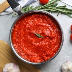 a pan filled with marinara sauce on top of a cutting board next to garlic and tomatoes