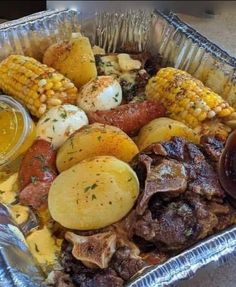 an aluminum pan filled with meat, potatoes and corn on the cob